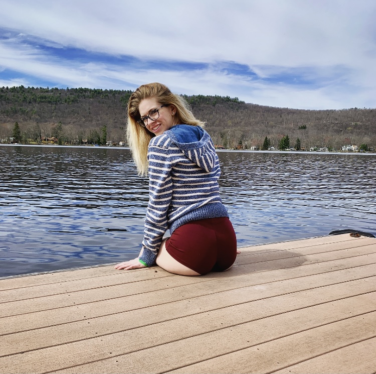 blonde girl sitting on the edge of a dock, dangling legs in the water