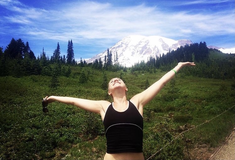 girl smiling with arms flung out in front of Mt. Rainier in Washington state