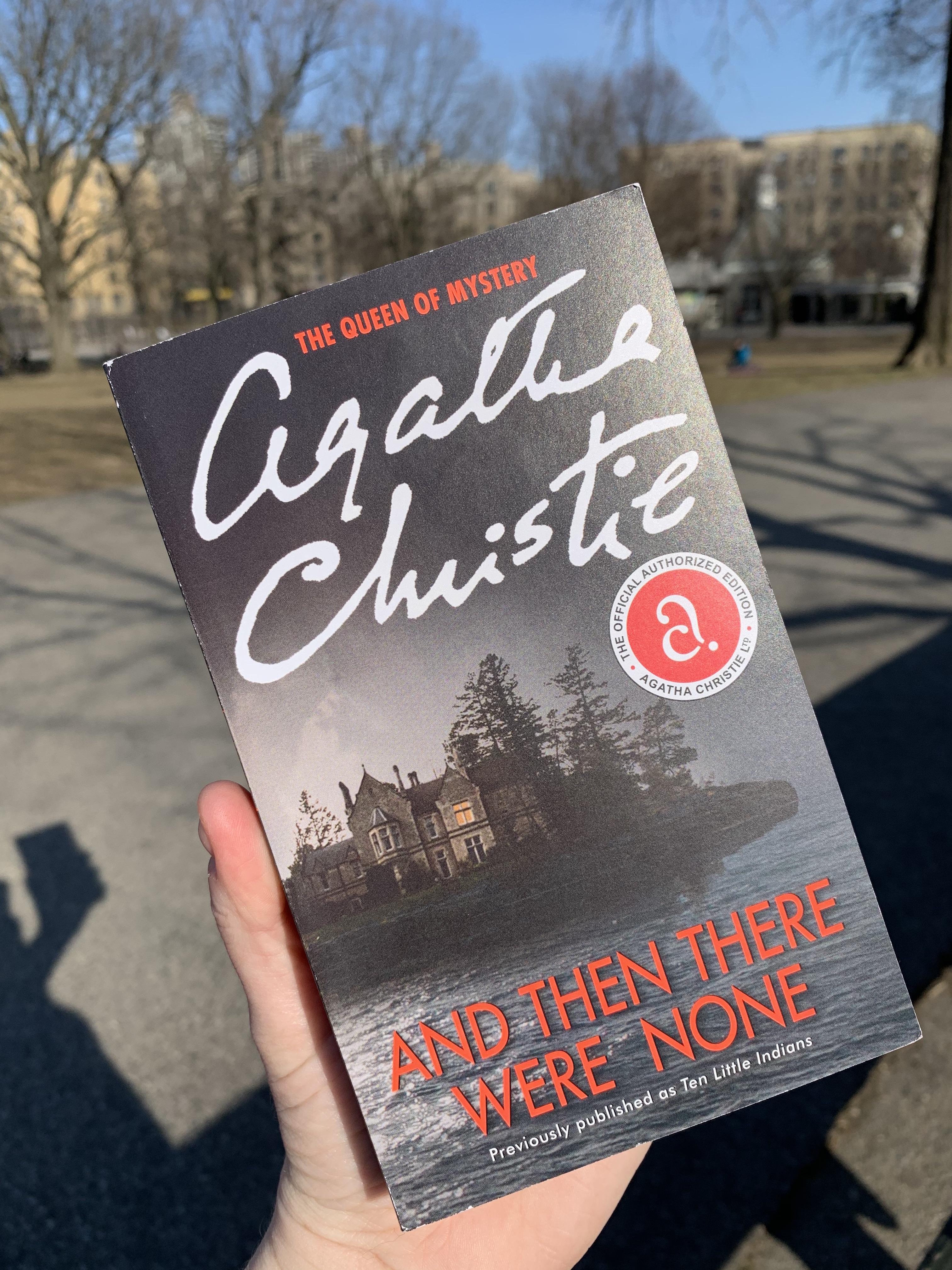 Agatha Christie book And Then There Were None, being held up to read in the park