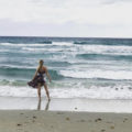 blonde girl in a sundress standing on Delray Beach facing the waves