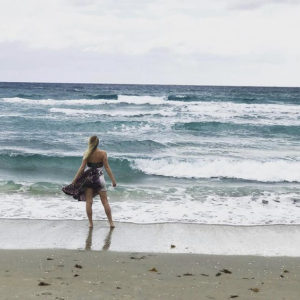 blonde girl in a sundress standing on Delray Beach facing the waves