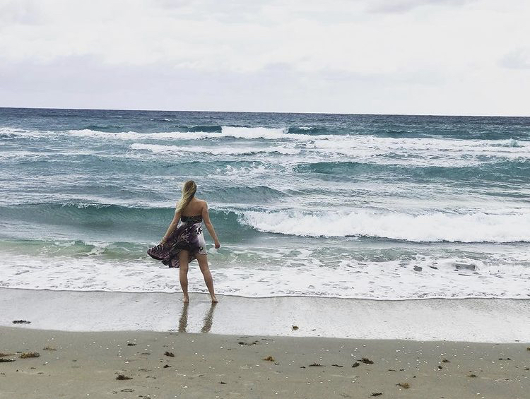 blonde girl in a sundress standing on Delray Beach facing the waves