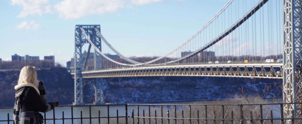 blonde woman facing away from the camera, looking at the George Washington Bridge in NYC
