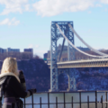 blonde woman facing away from the camera, looking at the George Washington Bridge in NYC