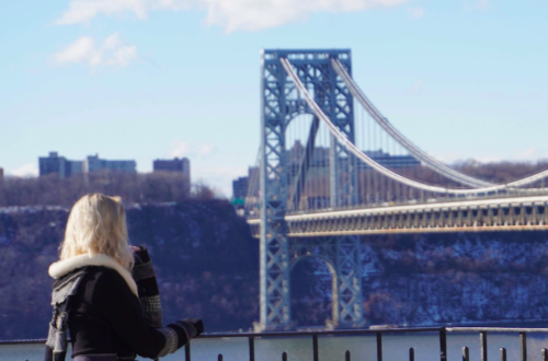 blonde woman facing away from the camera, looking at the George Washington Bridge in NYC