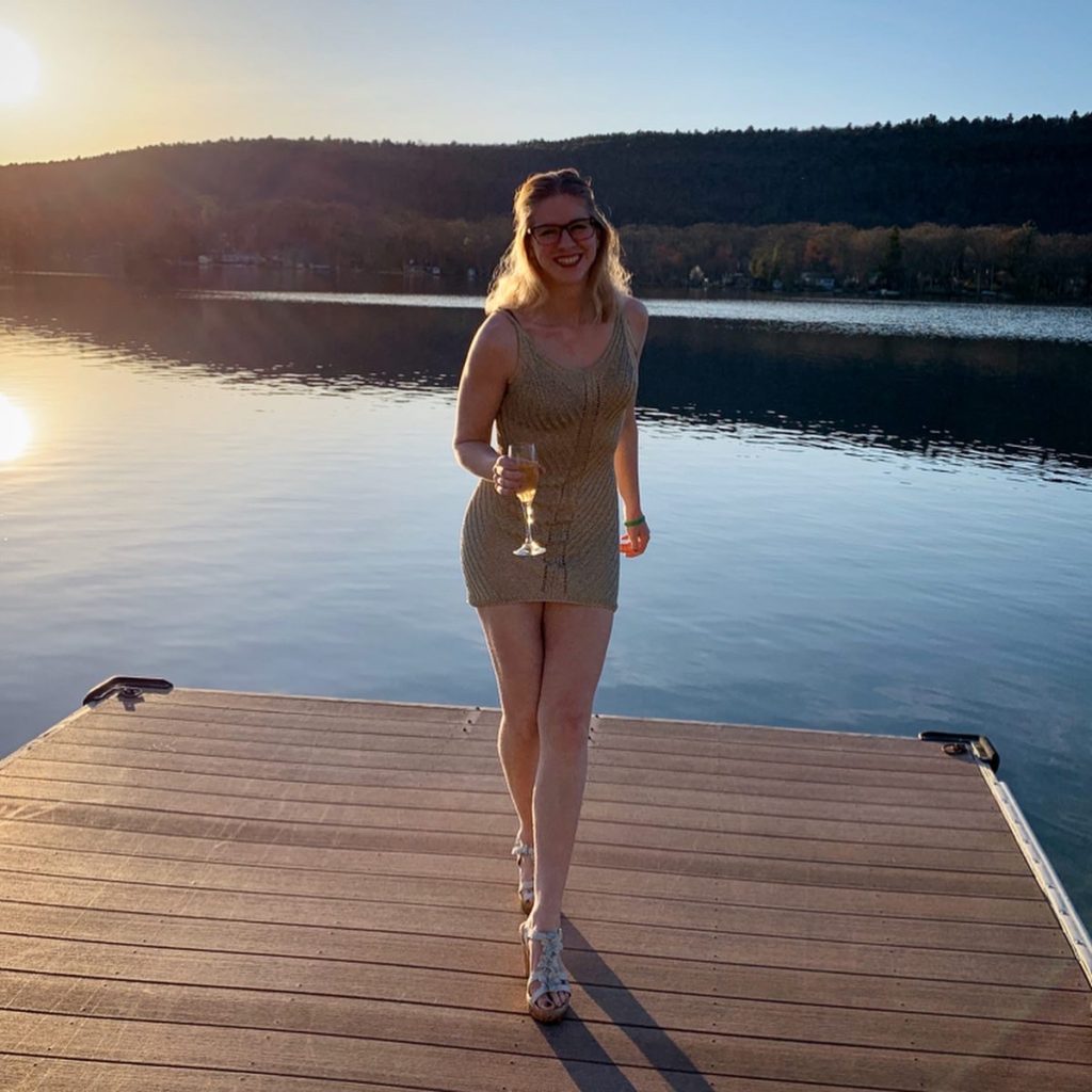 blonde girl celebrating her birthday with a glass of Red Bull, smiling at the camera on a dock in front of a lake