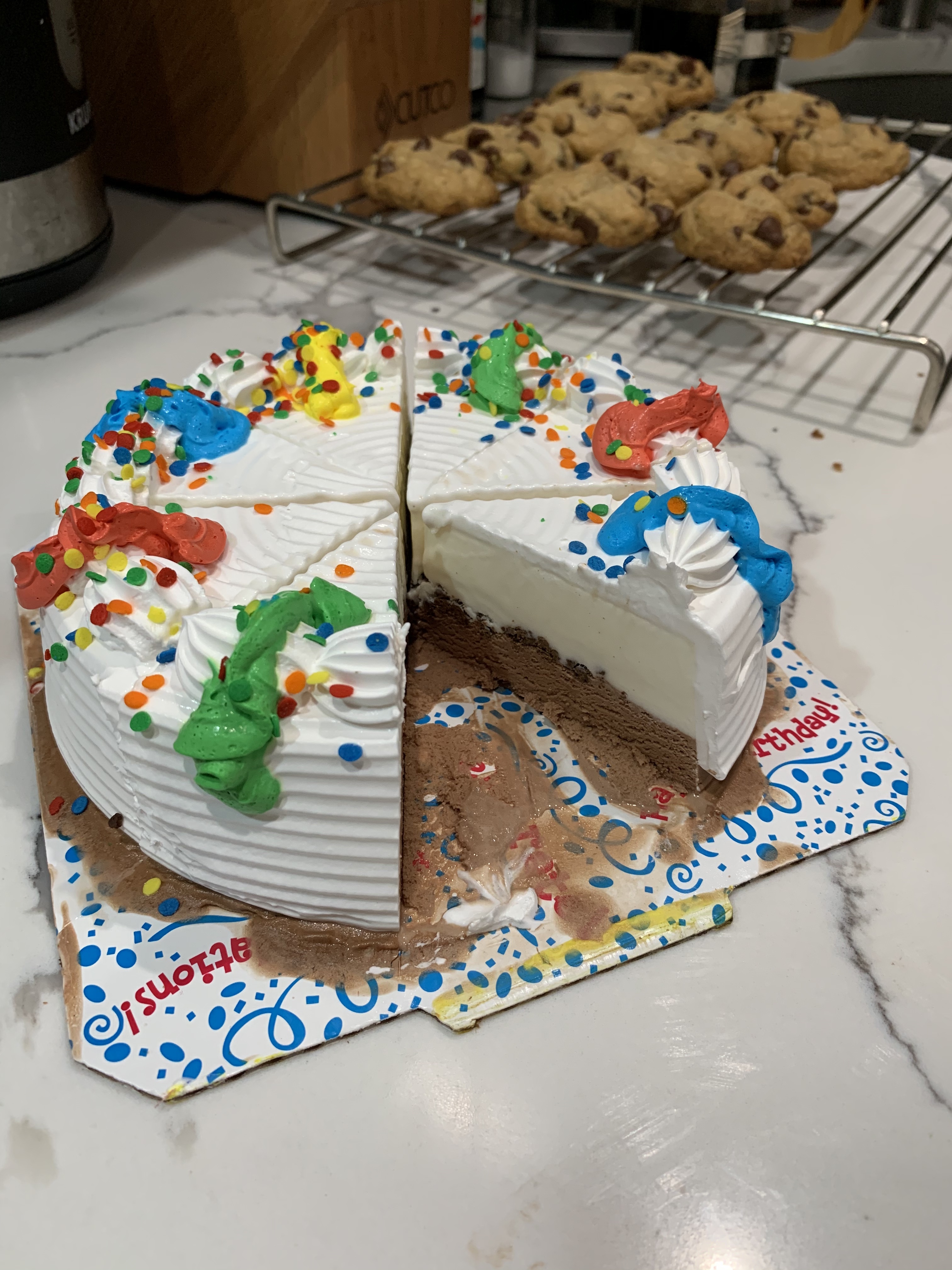 Carvel brand ice cream cake with vanilla and chocolate ice cream, cake is sliced with chocolate chip cookies in the background