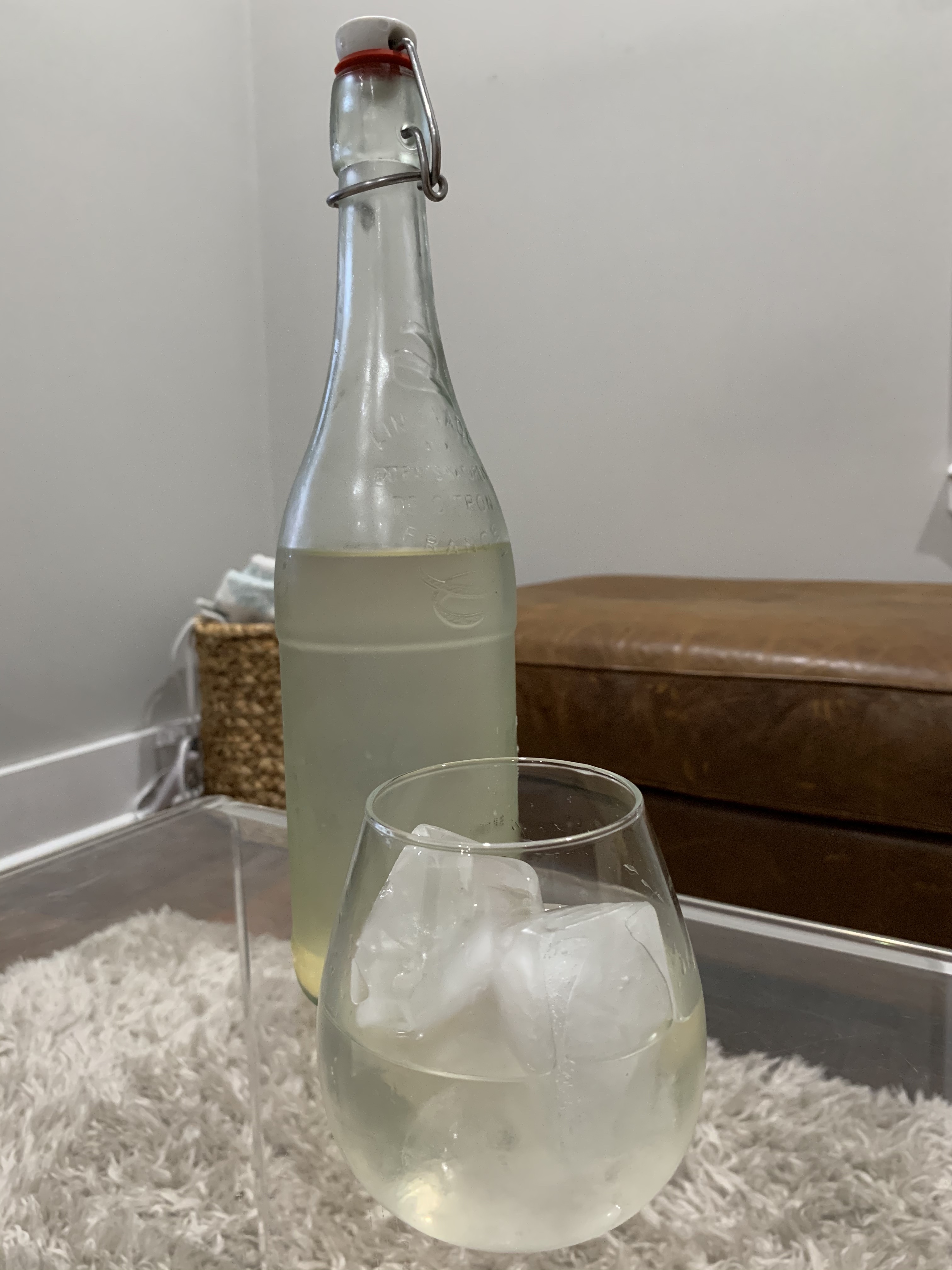 tall glass bottle filled with home-brewed ginger beer and a glass next to it with ice 