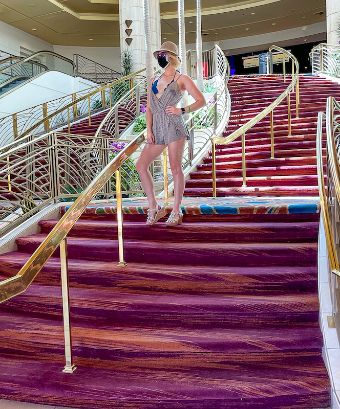 girl with a wide brim hat and purple aviators on standing in the middle of a staircase looking out