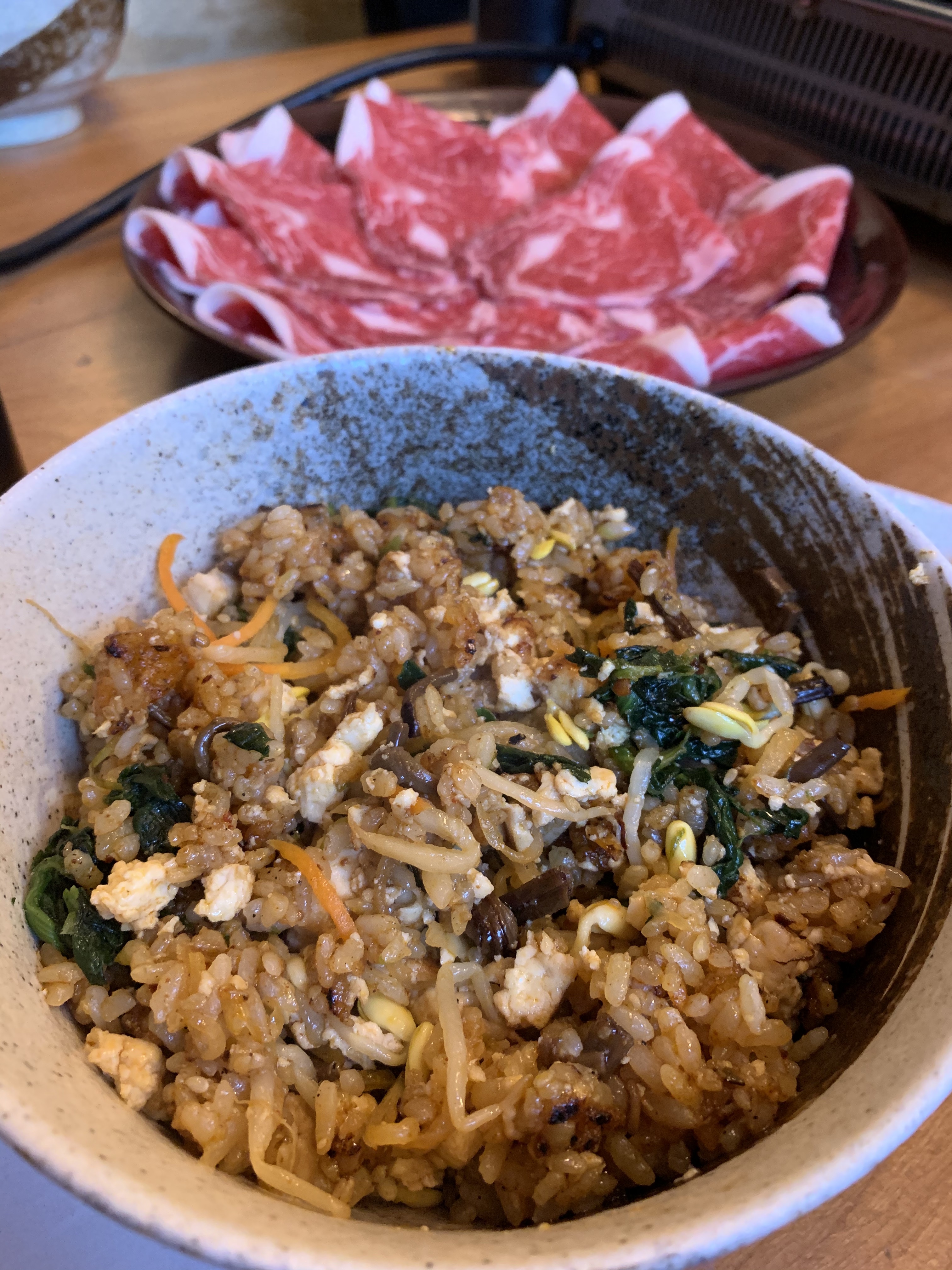 tofu bibim bap in a bowl, sliced uncooked beef in the background