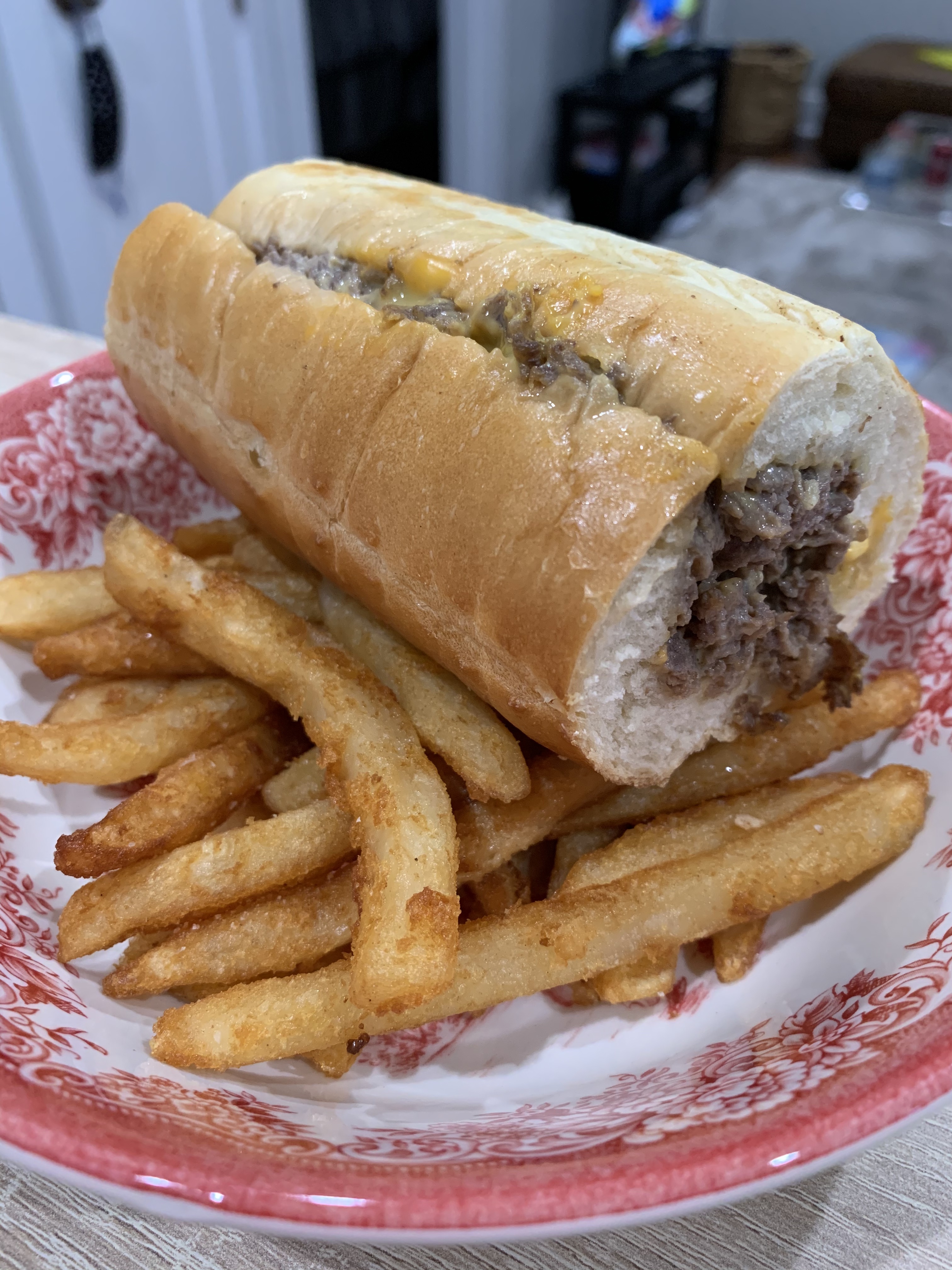 Philly cheesesteak sitting atop a bed of fries in a red and white patterned bowl