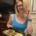 blonde girl in a blue top smiling at the camera and holding up a black to go container of food- mashed potatoes and chicken in the Venetian resort (Las Vegas)