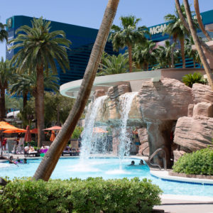 view of waterfall and palm trees at the MGM Grand Las Vegas pool deck, hotel visible in the background