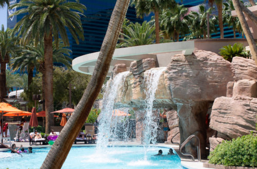 view of waterfall and palm trees at the MGM Grand Las Vegas pool deck, hotel visible in the background