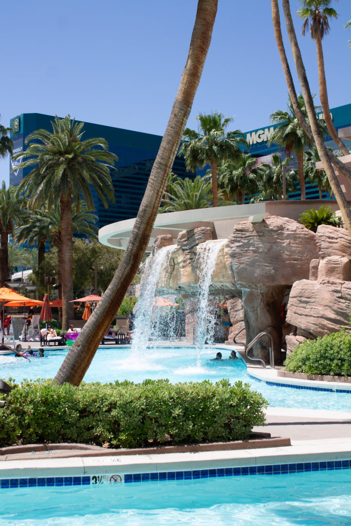 view of waterfall and palm trees at the MGM Grand pool deck, hotel visible in the background