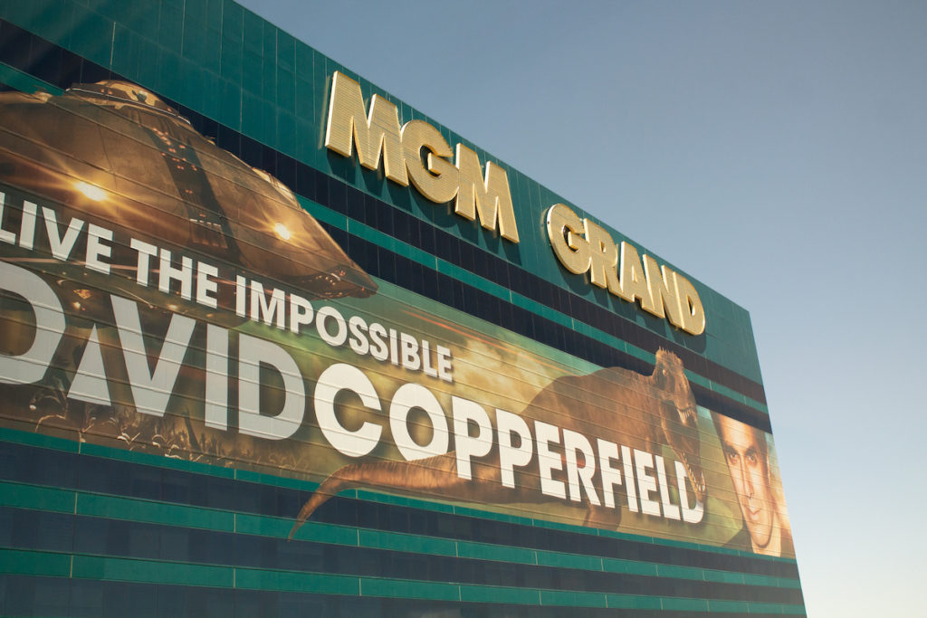 Exterior shot of the MGM Grand Las Vegas, big ad for David Copperfield's magic show, features his face, a T-Rex, and a UFO