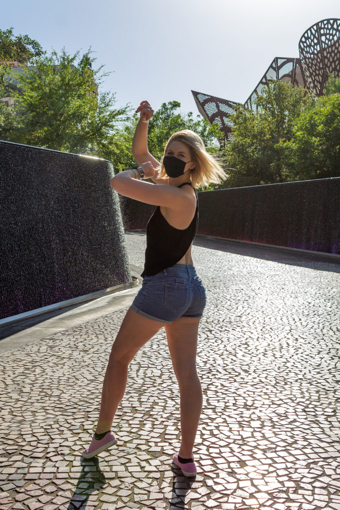 blonde girl with short hair wearing jean shorts a black top and a black mask, dancing on the street in Vegas