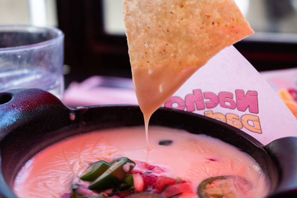 Chip dipping into a melted queso dip in a black bowl with jalapeños on top