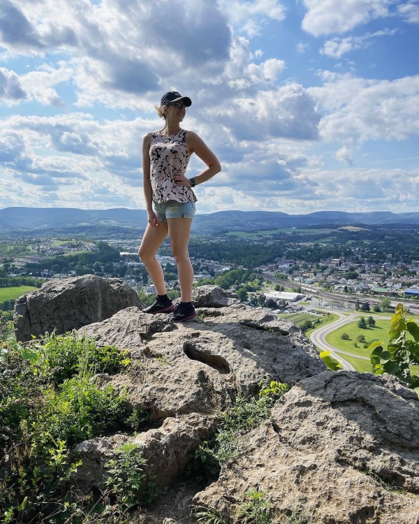 girl with short hair and a baseball cap on, standing at an overlook in Altoona, PA and looking off over the horizon with a smile