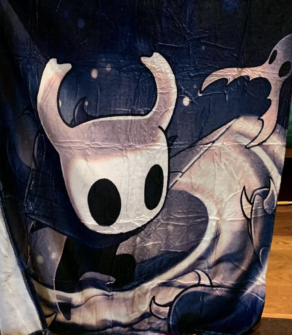 Hollow Knight video game blanket, dark blue background with the Knight with a white skull and big empty eyes slashing a nail