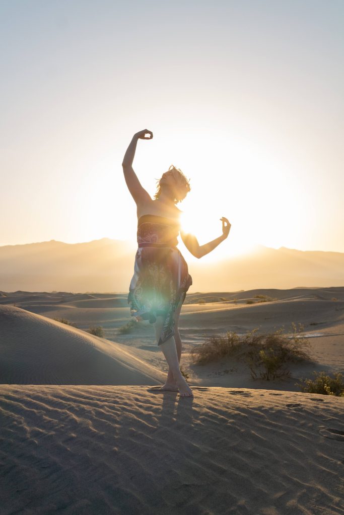 dancing girl, silhouetted by the sun, standing on sand dunes