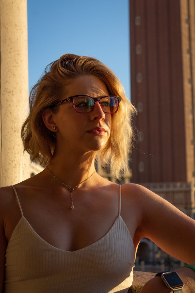 blonde girl with pink glasses looking out of frame, wearing a white tank top and a Fitbit